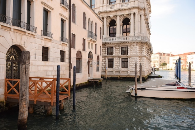 Un ampio canale nella Venezia italiana tra antichi edifici, illuminati dal sole, con barche su di esso.