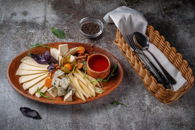 Un antipasto in un ristorante, un assortimento di formaggi. Formaggio a fette a strati su un piatto con verdure contro un tavolo di pietra grigia