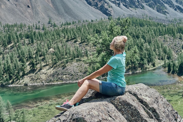 Un'anziana donna bionda siede su una pietra in alta montagna e si affaccia su una bellissima vista