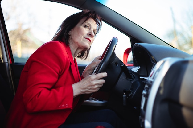 Un'anziana donna d'affari sta guidando la sua auto. Fa capolino sulla strada principale