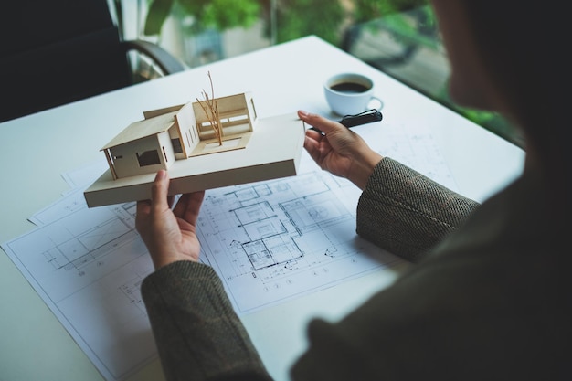 Un architetto che tiene e lavora su un modello di casa di architettura con carta da disegno per negozio in ufficio