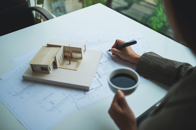 Un architetto donna che lavora su un modello di casa di architettura con carta da disegno per negozio in ufficio