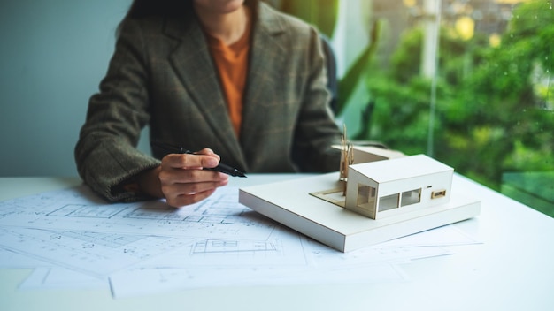 Un architetto donna che tiene e lavora su un modello di casa di architettura con carta da disegno per negozio in ufficio