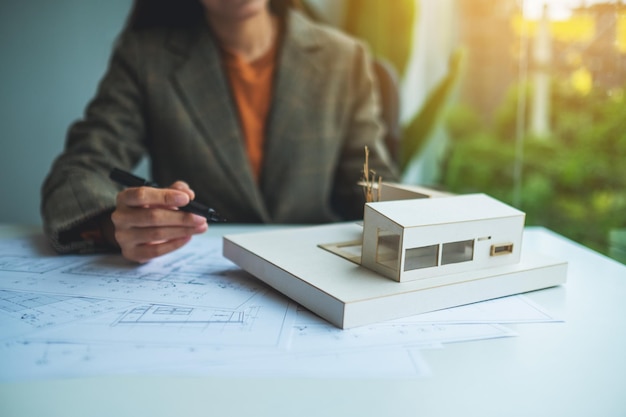 Un architetto donna che tiene e lavora su un modello di casa di architettura con carta da disegno per negozio in ufficio