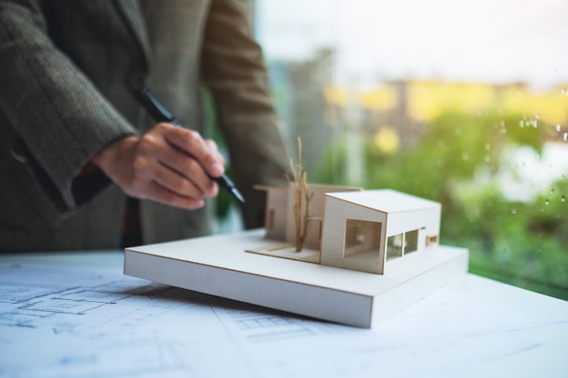 Un architetto donna che tiene e lavora su un modello di casa di architettura con carta da disegno per negozio in ufficio