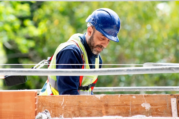 Un artigiano con un casco e una cintura di sicurezza applica una miscela di cemento con una spatola a un mattone