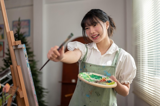 Un'artista asiatica creativa che tiene in mano un pennello e una tavolozza di colori mentre si trova in studio