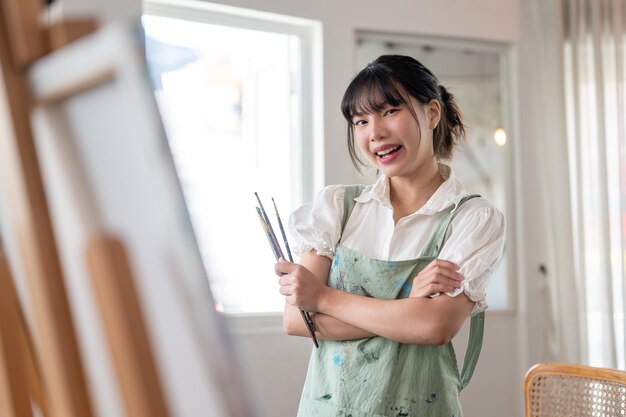 Un'artista sta con le braccia incrociate e tiene i pennelli in mano nel suo studio