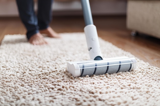 Un aspirapolvere senza fili pulisce il tappeto del soggiorno con la parte inferiore delle gambe. Tecnologie moderne per la pulizia della casa