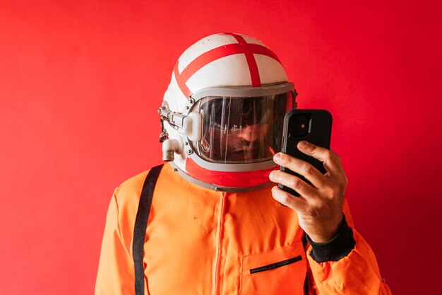 Un astronauta con un casco e una tuta spaziale arancione che scorre sul suo telefono su uno sfondo rosso