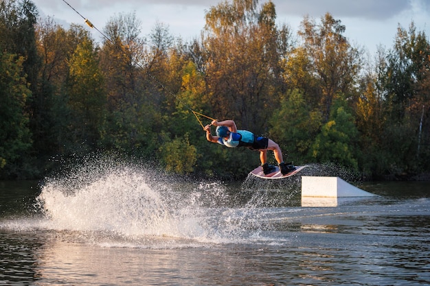 Un atleta fa un'acrobazia sull'acqua Un ciclista salta su un wakeboard sullo sfondo di una foresta verde Tramonto sul lago