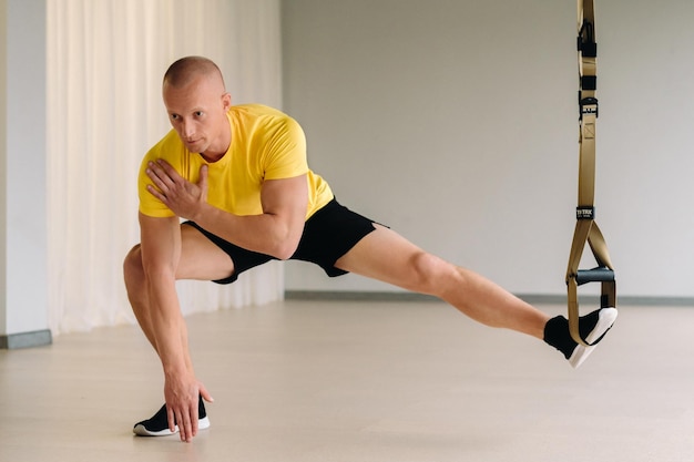 Un atleta maschio concentrato che esegue un esercizio su anelli funzionali in palestra.