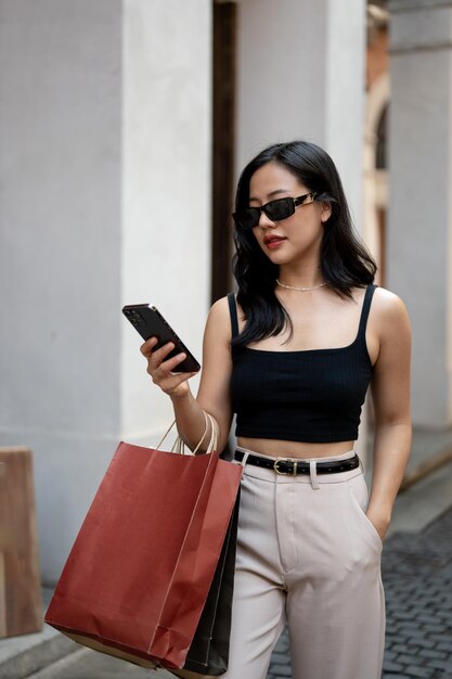 Un'attraente donna asiatica sta controllando i messaggi sul suo telefono mentre cammina per la strada della città