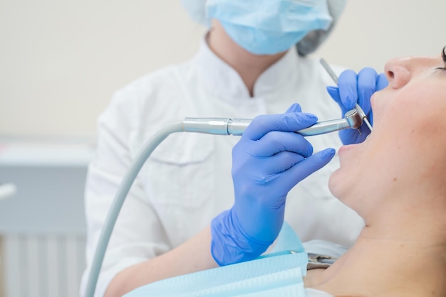 Un'attraente dottoressa sorridente in uniforme bianca esamina una paziente dai capelli rossi Il dentista produce tratta i denti con un trapano Primo piano