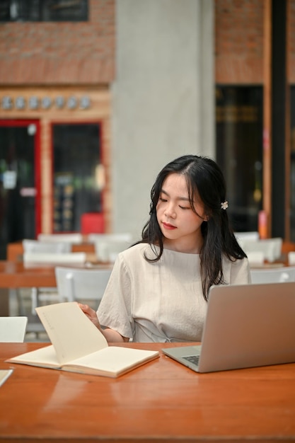 Un'attraente freelance asiatica si concentra sul suo lavoro lavorando a distanza in un bar