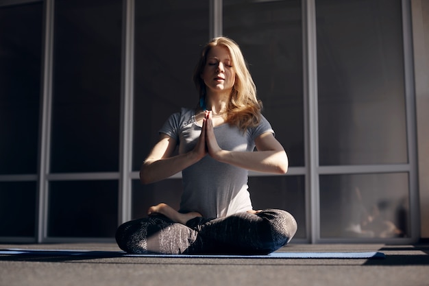 Un'attraente ragazza bionda in abiti sportivi medita durante le lezioni di yoga. Il concetto di uno stile di vita sano. Vista frontale