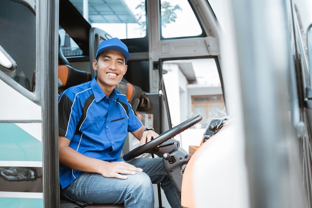 Un autista maschio in uniforme sorride mentre è seduto al volante dell'autobus