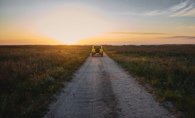 Un'auto che si muove lungo una strada della steppa di campagna alla luce di un bellissimo cielo al tramonto. Il concetto di viaggio ed esplorare la natura in auto