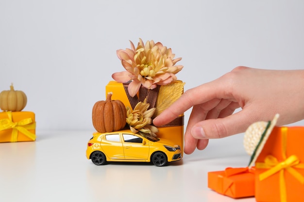 Un'auto giocattolo con una zucca un fiore e un regalo su uno sfondo chiaro