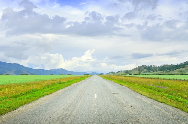 Un'autostrada rurale circondata da montagne in estate sotto un cielo nuvoloso blu. Siberia, Russia