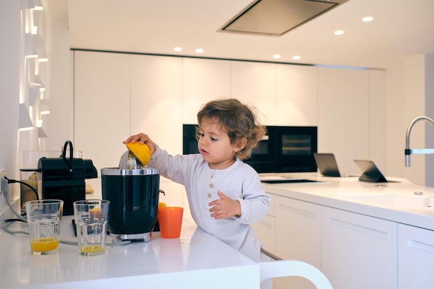 Un bambino adorabile in abiti casuali che prepara un delizioso succo d'arancia per una colazione sana in cucina domestica a casa