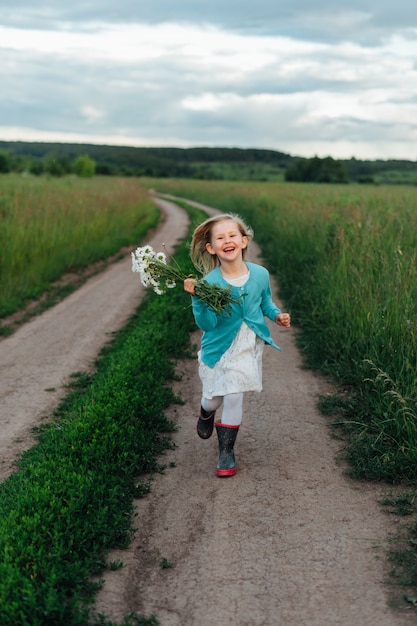 Un bambino allegro corre con un mazzo di margherite con gli stivali