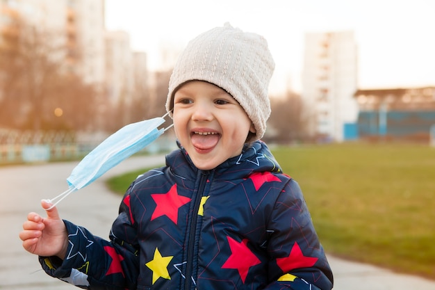 Un bambino allegro e gioioso per strada si toglie una mascherina medica dal viso. Felicità di respirare aria fresca durante una passeggiata dopo la quarantena. Sollevare le restrizioni. Bimbo felice.