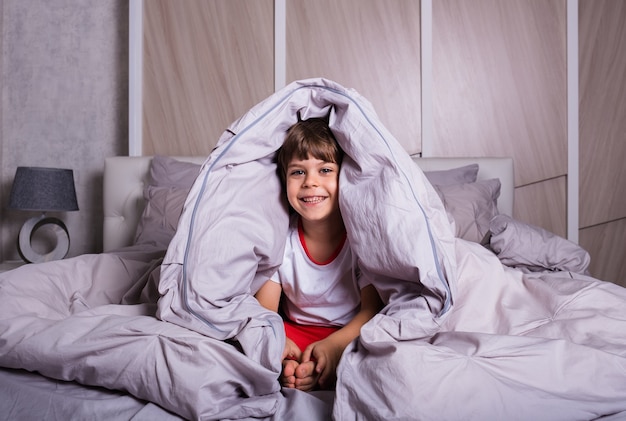 Un bambino allegro in pigiama è seduto su lenzuola di cotone sul letto