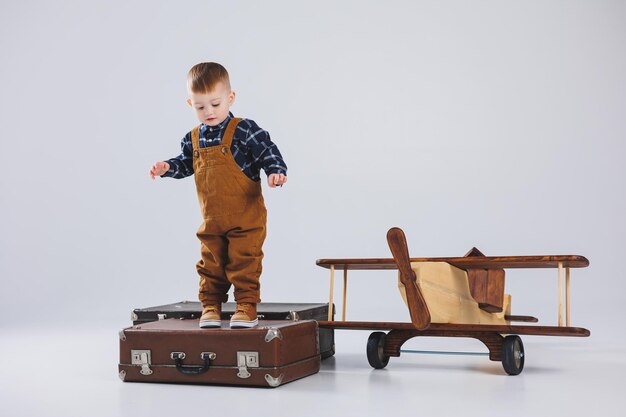 Un bambino allegro in una tuta marrone è in piedi su una valigia Piccolo viaggiatore con una valigia Giocattoli ecologici per bambini in legno aereo