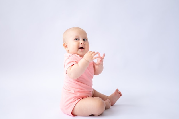 Un bambino allegro in una tuta rosa è seduto su uno sfondo bianco il bambino sta sorridendo isolato