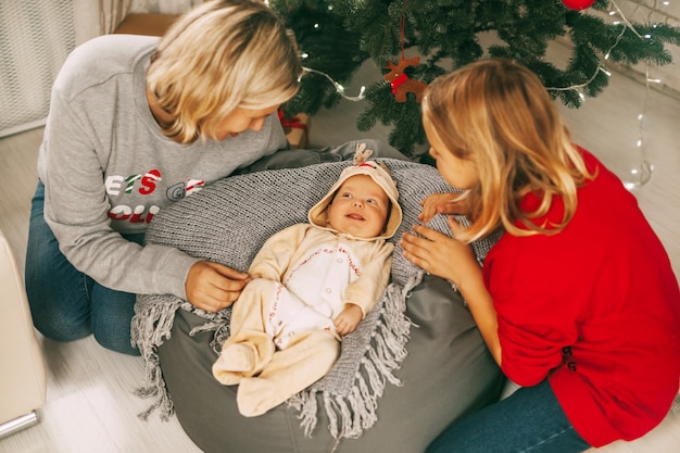 Un bambino allegro si trova accanto all'albero di Natale e sorride a sua madre e sua sorella.