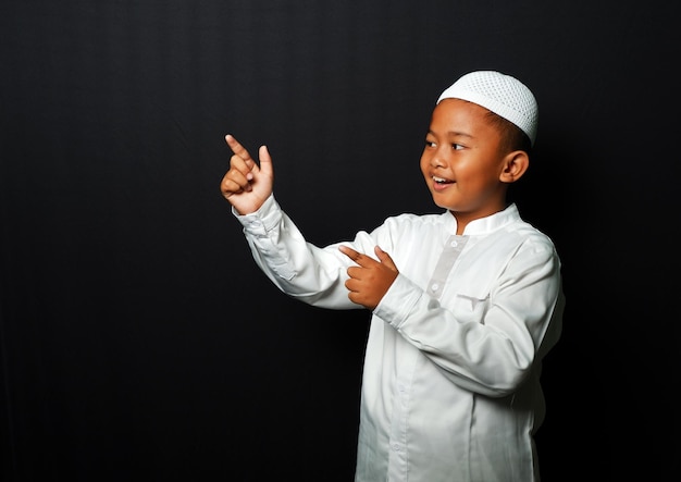 Un bambino asiatico che indossa un berretto punta la mano verso lo spazio vuoto isolato su sfondo nero