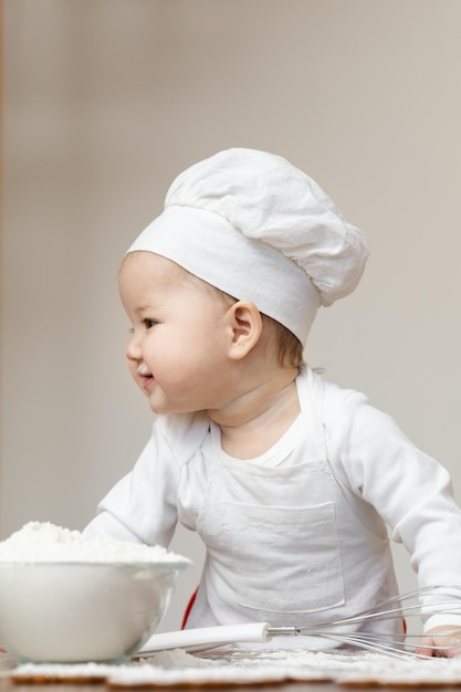 Un bambino asiatico in berretto da chef e grembiule spalmato di farina prepara i biscotti allo zenzero di Natale