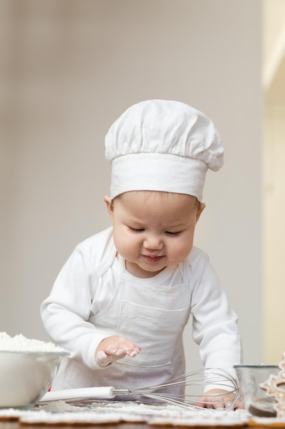 Un bambino asiatico in berretto da chef e grembiule spalmato di farina prepara i biscotti allo zenzero di Natale