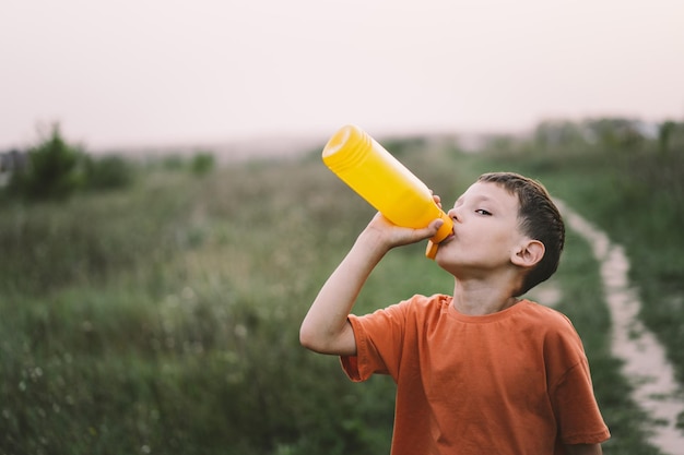 Un bambino beve acqua da una bottiglia arancione mentre cammina per la salute del bambino