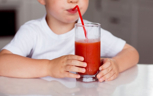 Un bambino beve succo rosso da un bicchiere