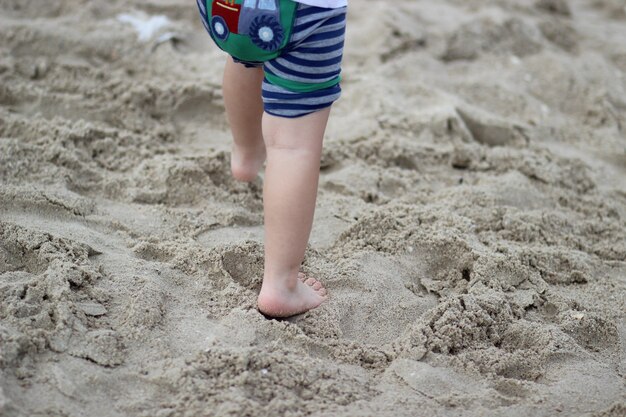 Un bambino cammina lungo la spiaggia in pantaloni con un trattore blu