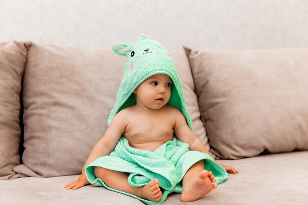 Un bambino carino avvolto in un asciugamano si siede sul letto. bambino in un asciugamano da bagno.