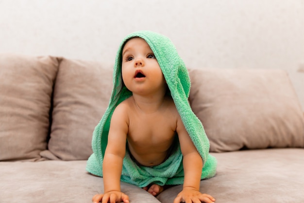 Un bambino carino avvolto in un asciugamano si siede sul letto. bambino in un asciugamano da bagno.