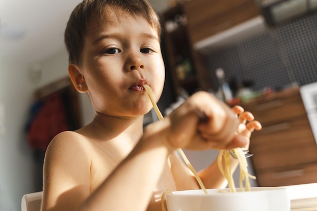 Un bambino carino che mangia il suo cibo preferito, gli spaghetti.