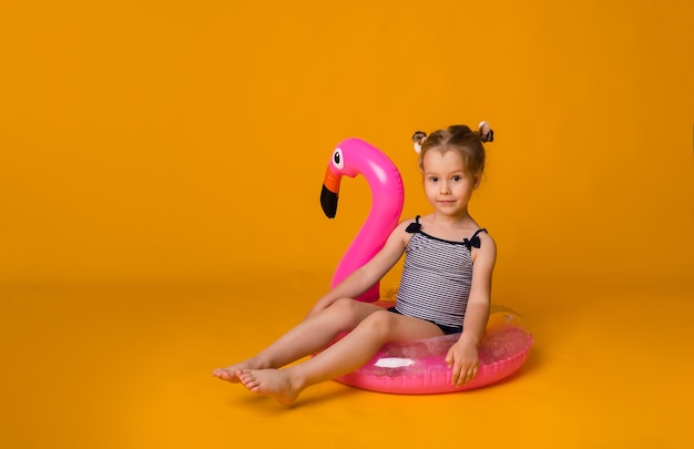 Un bambino carino con un costume da bagno a righe siede in un cerchio gonfiabile rosa e guarda la telecamera su uno sfondo giallo con spazio per il testo