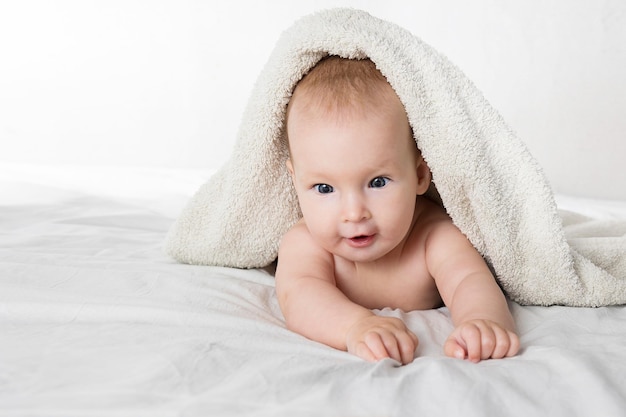 Un bambino carino di mezzo anno con un pannolino e un asciugamano giace sulla pancia e guarda allegramente la telecamera