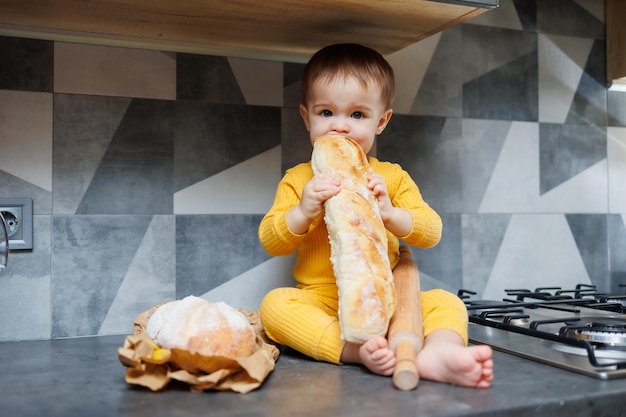 Un bambino carino di un anno si siede e mangia pane di segale appena sfornato Il bambino tiene in mano una baguette fresca