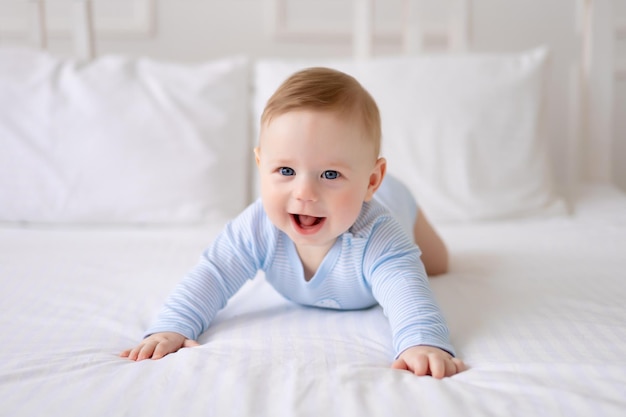 Un bambino carino e sano è sdraiato su un letto su lenzuola bianche a casa in un body blu Il bambino guarda la telecamera sorride