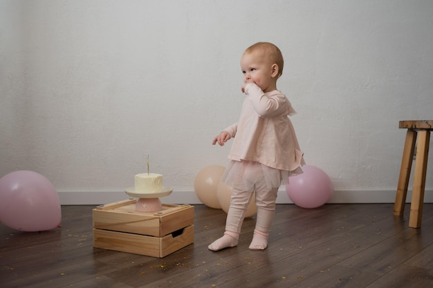 Un bambino carino festeggia il suo compleanno con una torta contro un muro bianco, una bambina in rosa è una