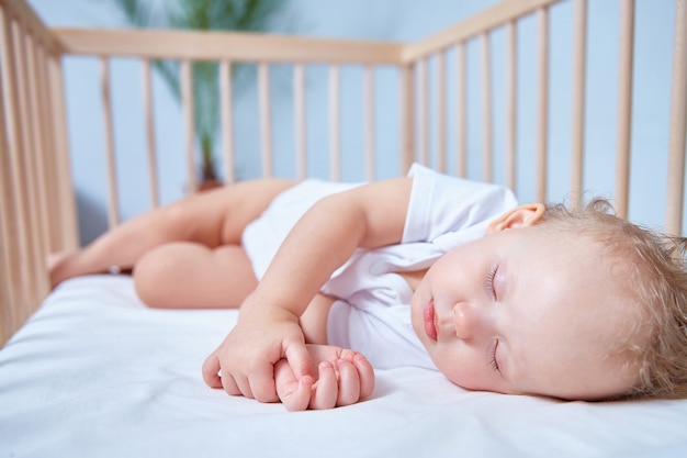 Un bambino carino in abiti bianchi dorme in una culla di legno in un luminoso