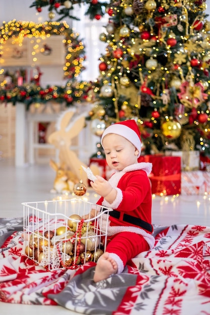 Un bambino carino in un costume da Babbo Natale è seduto con i giocattoli dell'albero di Natale