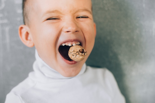 Un bambino cerca di rompere una noce mostrando denti da latte sani e forti, fa uno sforzo