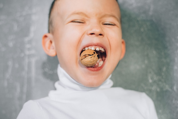 Un bambino cerca di rompere una noce mostrando denti da latte sani e forti, fa uno sforzo