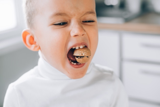 Un bambino cerca di rompere una noce mostrando denti da latte sani e forti, fa uno sforzo